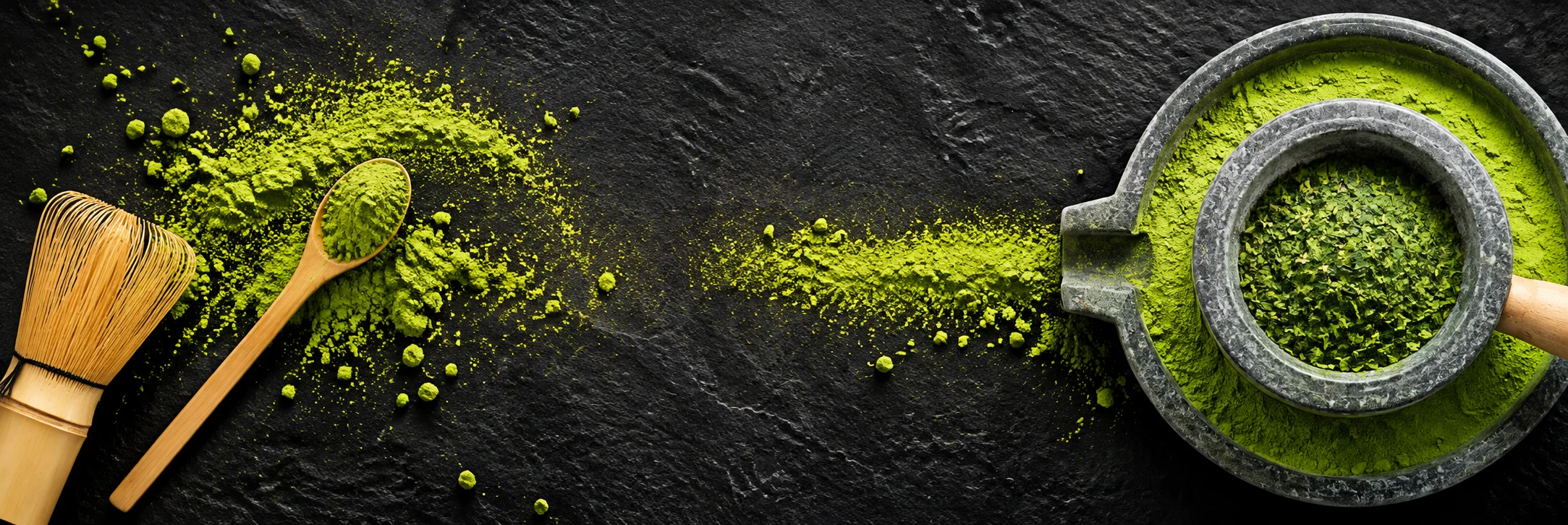 Matcha powder, bamboo whisk and stone mill on dark slate
